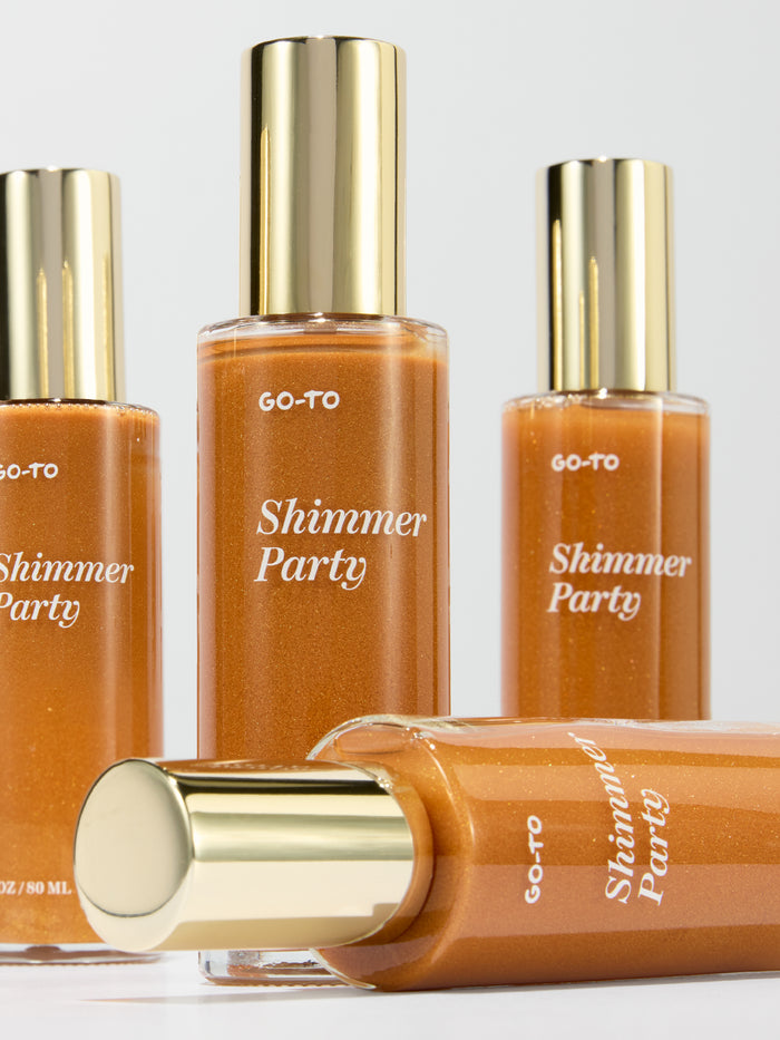 Go-To Skincare Shimmer Party body shimmer bottles in amber glass with reflective gold caps arranged on a light background with one bottle lying flat