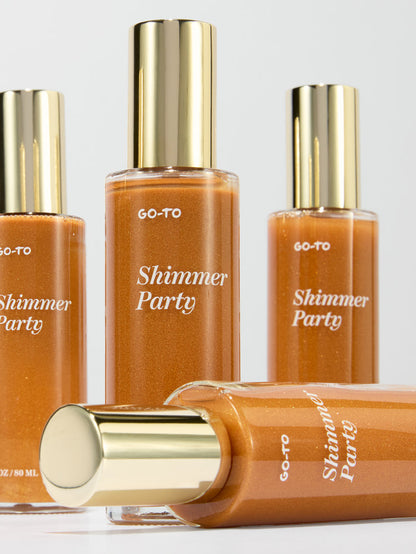 Go-To Skincare Shimmer Party body shimmer bottles in amber glass with reflective gold caps arranged on a light background with one bottle lying flat